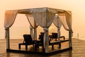 A gazebo with white curtains on the beach at sunset photo