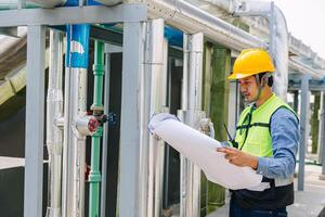 A man in a yellow helmet and a green vest is looking at a piece of paper. He is wearing a hard hat and he is a worker photo