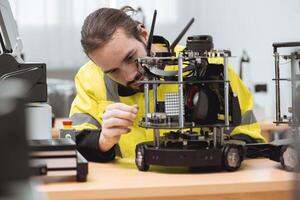 Engineer male education in Industrial Robotics program in university engineering lab classroom learning assembly and programming mobile robots electronic system. photo