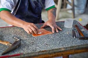 Closeup hands of leather craftsman is carefully to use a cotton swab soaked in water to wipe the leather sheet to make it soft for easy stamping design. photo