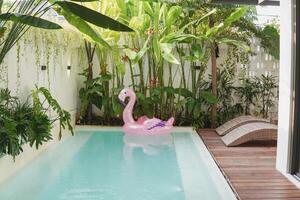 A pink inflatable flamingo floats in a pool. The pool is in a backyard, and there are two lounge chairs on the deck. photo