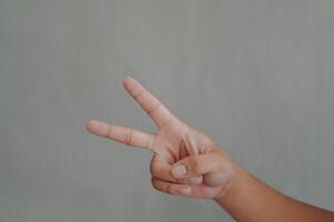 A hand is holding up two fingers, which is a symbol of peace, isolated over grey background. photo