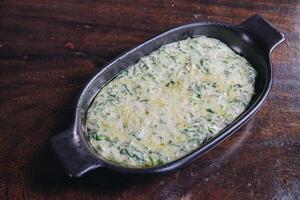 Delicious creamy spinach in a black bowl looks appetizing and inviting served on a wooden table. photo