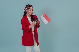 Happy Indonesian young woman holding a flag while using smartphone to browse internet. photo