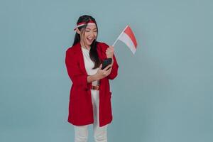 Excited Indonesian young woman holding a flag while using smartphone to browse internet. photo