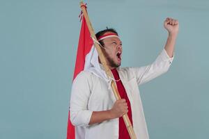 Energetic Indonesian man is holding a flag while raising fist gesture and shouting loud. photo