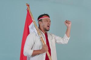 Energetic Indonesian man is holding a flag while raising fist gesture and shouting loud. photo