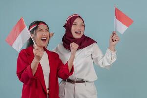 Two excited Indonesian women holding mini country flag smiling and giving support. photo