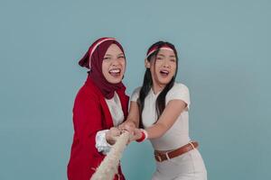 Two Indonesian woman struggling and pulling rope in a competition with shocked expression. photo