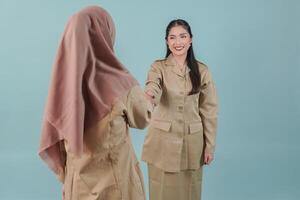 Two smiling Indonesian government worker women wearing khaki uniform doing handshake gesture. photo