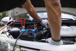 mechanic from the service center is helping to jump start the car battery for customer who has a deteriorated battery and cannot start the car. Jump starting the battery helps to continue the journey photo