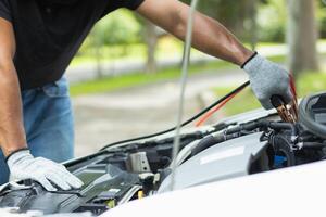 mechanic from the service center is helping to jump start the car battery for customer who has a deteriorated battery and cannot start the car. Jump starting the battery helps to continue the journey photo