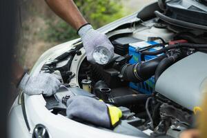 mechanic is checking car and adding water to radiator to increase the engine cooling capacity. mechanic from the service center who was called by service center application is helping customer photo