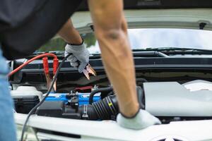 mechanic from the service center is helping to jump start the car battery for customer who has a deteriorated battery and cannot start the car. Jump starting the battery helps to continue the journey photo