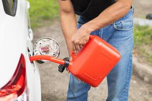 young man holds red gallon of gasoline which is reserve gasoline for emergency use when running out of fuel during trip or using reserve gasoline in red gallon to help people who run out of fuel. photo
