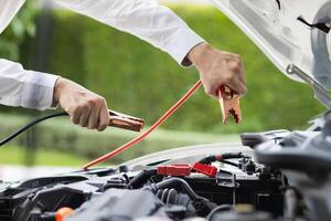 mechanic from the service center is helping to jump start the car battery for customer who has a deteriorated battery and cannot start the car. Jump starting the battery helps to continue the journey photo