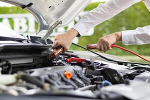 mechanic from the service center is helping to jump start the car battery for customer who has a deteriorated battery and cannot start the car. Jump starting the battery helps to continue the journey photo