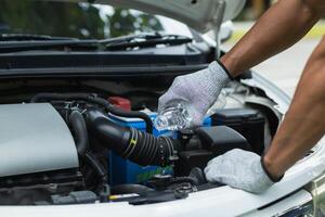 mechanic is checking car and adding water to radiator to increase the engine cooling capacity. mechanic from the service center who was called by service center application is helping customer photo