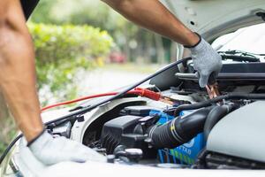 mechanic from the service center is helping to jump start the car battery for customer who has a deteriorated battery and cannot start the car. Jump starting the battery helps to continue the journey photo