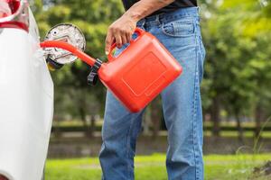 young man holds red gallon of gasoline which is reserve gasoline for emergency use when running out of fuel during trip or using reserve gasoline in red gallon to help people who run out of fuel. photo