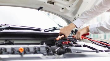 mechanic from the service center is helping to jump start the car battery for customer who has a deteriorated battery and cannot start the car. Jump starting the battery helps to continue the journey photo