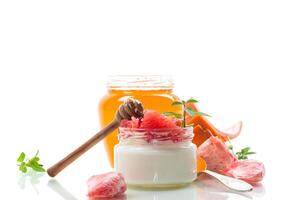 homemade sweet yogurt in a glass jar with pieces of red ripe grapefruit and honey, isolated on white background photo