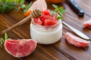 homemade sweet yogurt in a glass jar with pieces of red ripe grapefruit and honey, on a wooden table photo