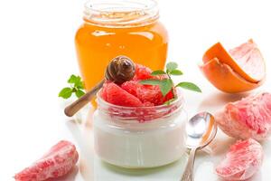 homemade sweet yogurt in a glass jar with pieces of red ripe grapefruit and honey, isolated on white background photo