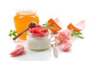homemade sweet yogurt in a glass jar with pieces of red ripe grapefruit and honey, isolated on white background photo