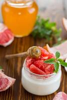homemade sweet yogurt in a glass jar with pieces of red ripe grapefruit and honey, on a wooden table photo