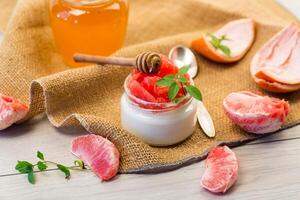 homemade sweet yogurt in a glass jar with pieces of red ripe grapefruit and honey, on a wooden table photo