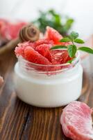 homemade sweet yogurt in a glass jar with pieces of red ripe grapefruit and honey, on a wooden table photo