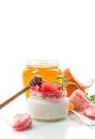 homemade sweet yogurt in a glass jar with pieces of red ripe grapefruit and honey, isolated on white background photo
