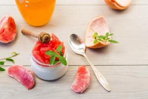 homemade sweet yogurt in a glass jar with pieces of red ripe grapefruit and honey, on a wooden table photo