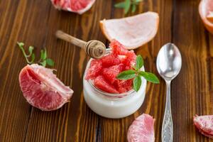 homemade sweet yogurt in a glass jar with pieces of red ripe grapefruit and honey, on a wooden table photo