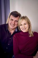 attractive middle-aged married couple hugging and smiling on sofa, studio photo shoot