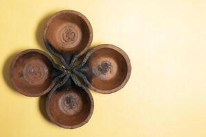 Close-up view of four traditional mud diyas arranged in floral pattern on yellow background with copy space. photo