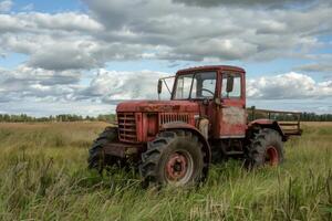 Old red tractor resting in a grass field under a cloudy sky photo