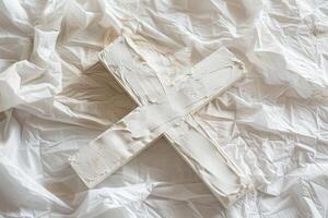 White wooden cross lying on crumpled paper covered in dried paint photo