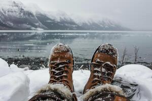 Hiker resting with snow covered boots in front of scenic mountain lake photo