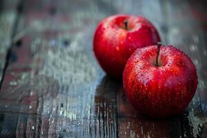Two fresh, wet, red apples are sitting on a rustic wood surface photo