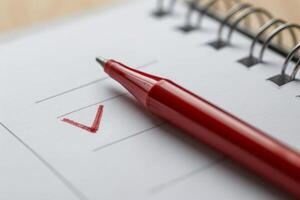 Red pen marking check mark on checklist in notepad photo