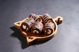 Chocolate roll cake with fresh cream in wooden plate isolated on dark background. chocolate swiss roll cake. top view. photo