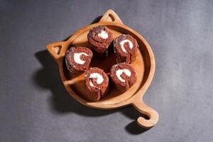 Chocolate roll cake with fresh cream in wooden plate isolated on dark background. chocolate swiss roll cake. top view. photo
