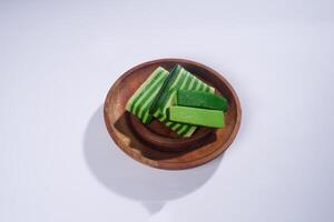 Sticky layer cake or Kue Lapis on wooden plate isolated on white background. Indonesian traditional dessert made from rice flour and coconut milk, steamed layer by layer served on banana leaves. photo
