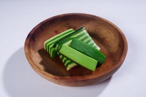 Sticky layer cake or Kue Lapis on wooden plate isolated on white background. Indonesian traditional dessert made from rice flour and coconut milk, steamed layer by layer served on banana leaves. photo