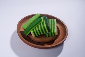 Sticky layer cake or Kue Lapis on wooden plate isolated on white background. Indonesian traditional dessert made from rice flour and coconut milk, steamed layer by layer served on banana leaves. photo