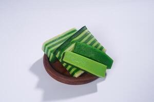 Sticky layer cake or Kue Lapis on wooden plate isolated on white background. Indonesian traditional dessert made from rice flour and coconut milk, steamed layer by layer served on banana leaves. photo