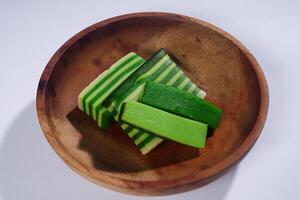 Sticky layer cake or Kue Lapis on wooden plate isolated on white background. Indonesian traditional dessert made from rice flour and coconut milk, steamed layer by layer served on banana leaves. photo