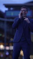 A man dressed in a suit is engaged in an animated conversation on the phone during dusk video